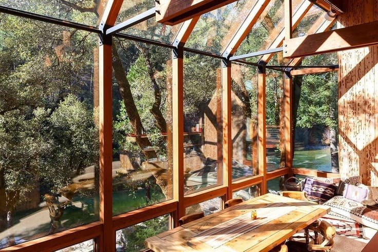 Wood-framed glass sunroom with forest views and cozy dining nook