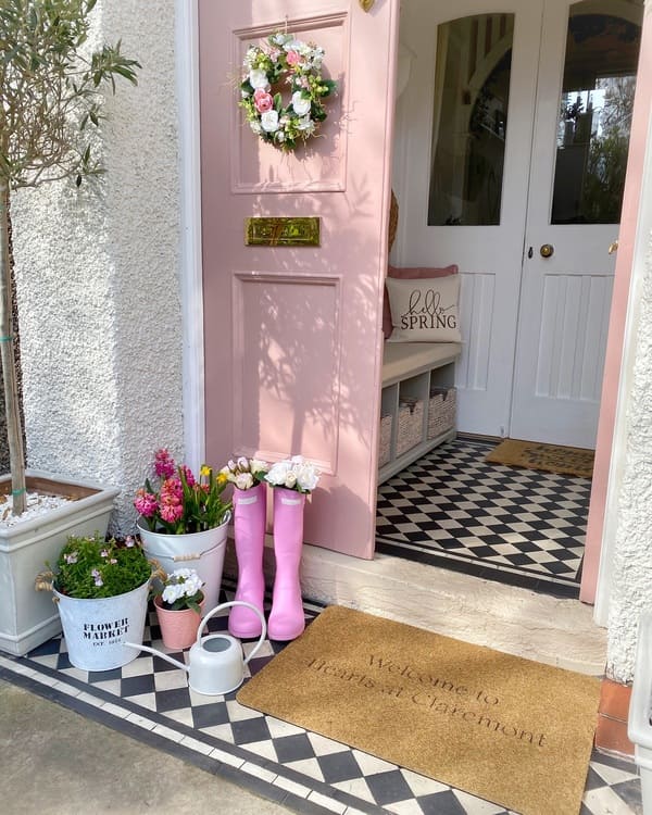 A Soft pink door with floral wreath, boots-as-planters and black-and-white checkered floor.