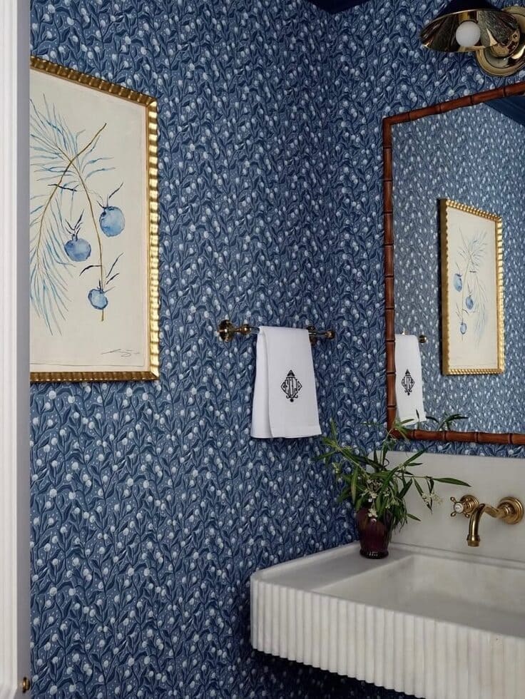 Blue patterned bathroom wallpaper with a fluted sink and gold fixtures