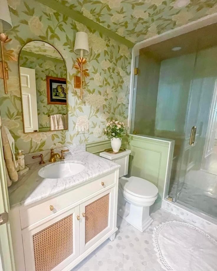 Soft green floral bathroom wallpaper with gold sconces and a marble vanity
