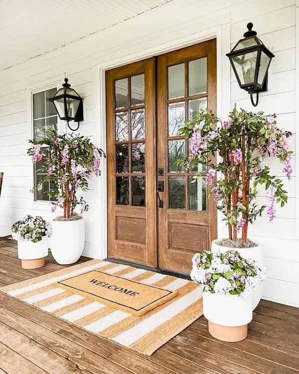 Double doors made from natural wood flanked by blooms resembling wisteria and crisp white planters.