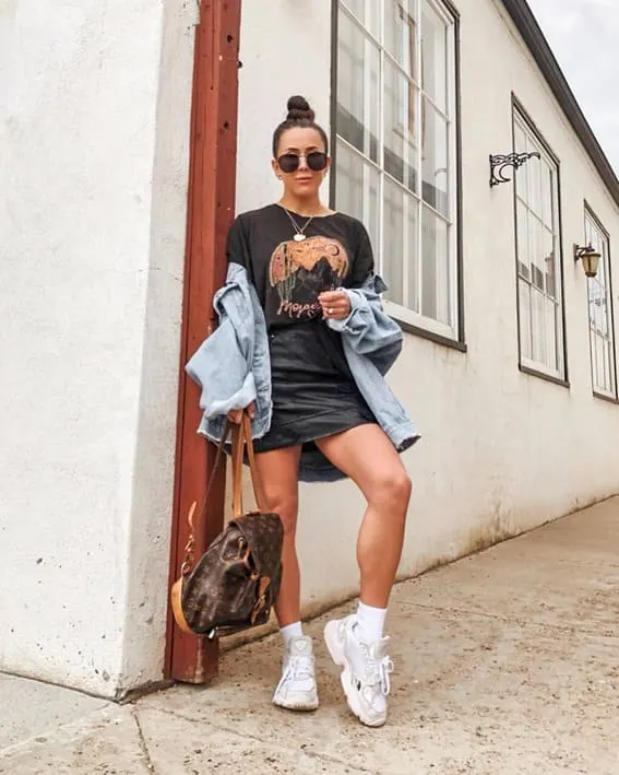A woman in a graphic tee and an denim jacket and a mini skirt.