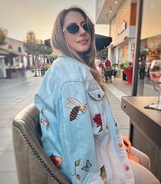 Woman wearing a light wash denim coat with flowers and bees