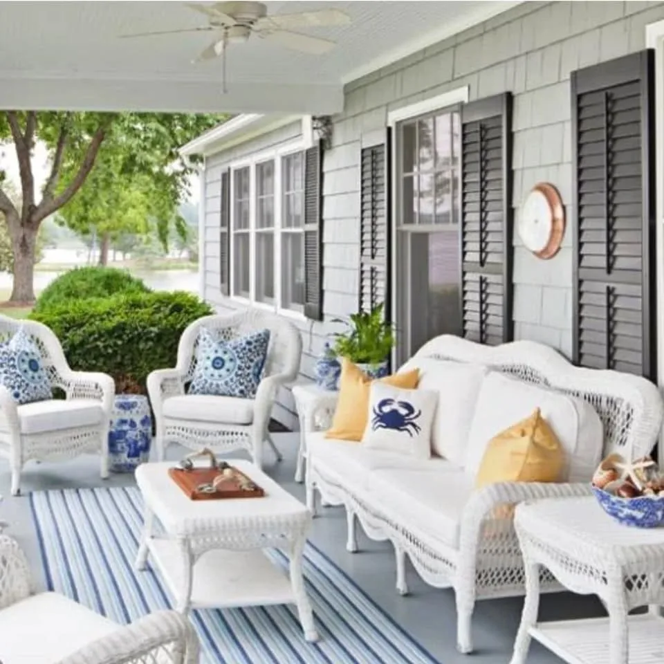 A breezy porch, with light blue floors, white wicker furniture, striped rugs and coastal-themed pillows in navy and yellow.