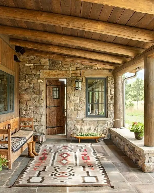 Front porch stone and log, bench made of wood, cowboy boots, tribal-style rug, earthy accents, in a natural setting.