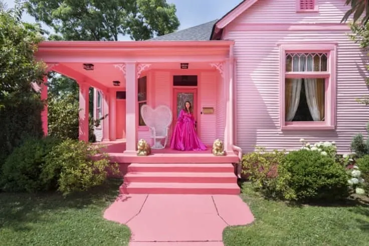 A grand pink porch featuring a woman in a pink gown, a heart-shaped chair, and two golden lion statues.