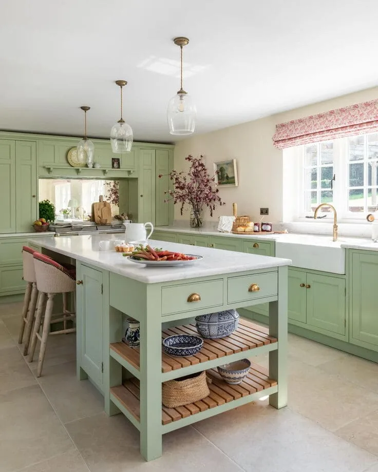Spacious kitchen with soft pastel green cabinets, central island with open shelving, white countertops, and brass fixtures