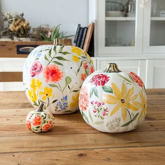 A beautiful trio of hand-painted pumpkins featuring vibrant floral designs in a mix of bright, cheerful colors.
