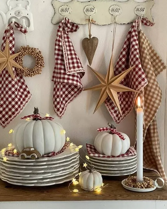 A cozy cottage-style display featuring white pumpkins, gingham linens, and star-shaped string lights for a rustic autumn vibe.