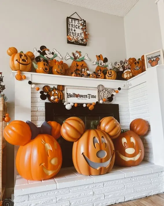 A playful mantel display featuring Mickey and Minnie-themed pumpkin decorations with garlands and Halloween accents.