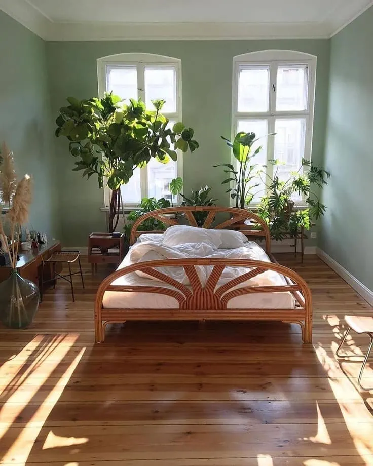 Minimalist bedroom with rattan bed frame, green walls, and lush plants